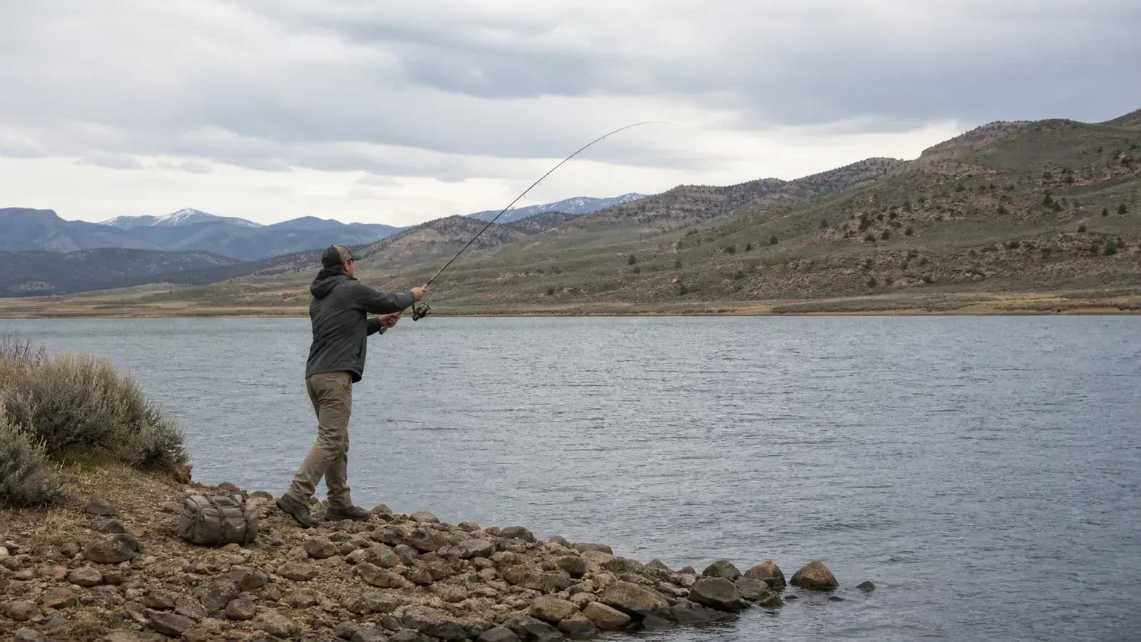 Angler casting a spinning rod from an open reservoir bank