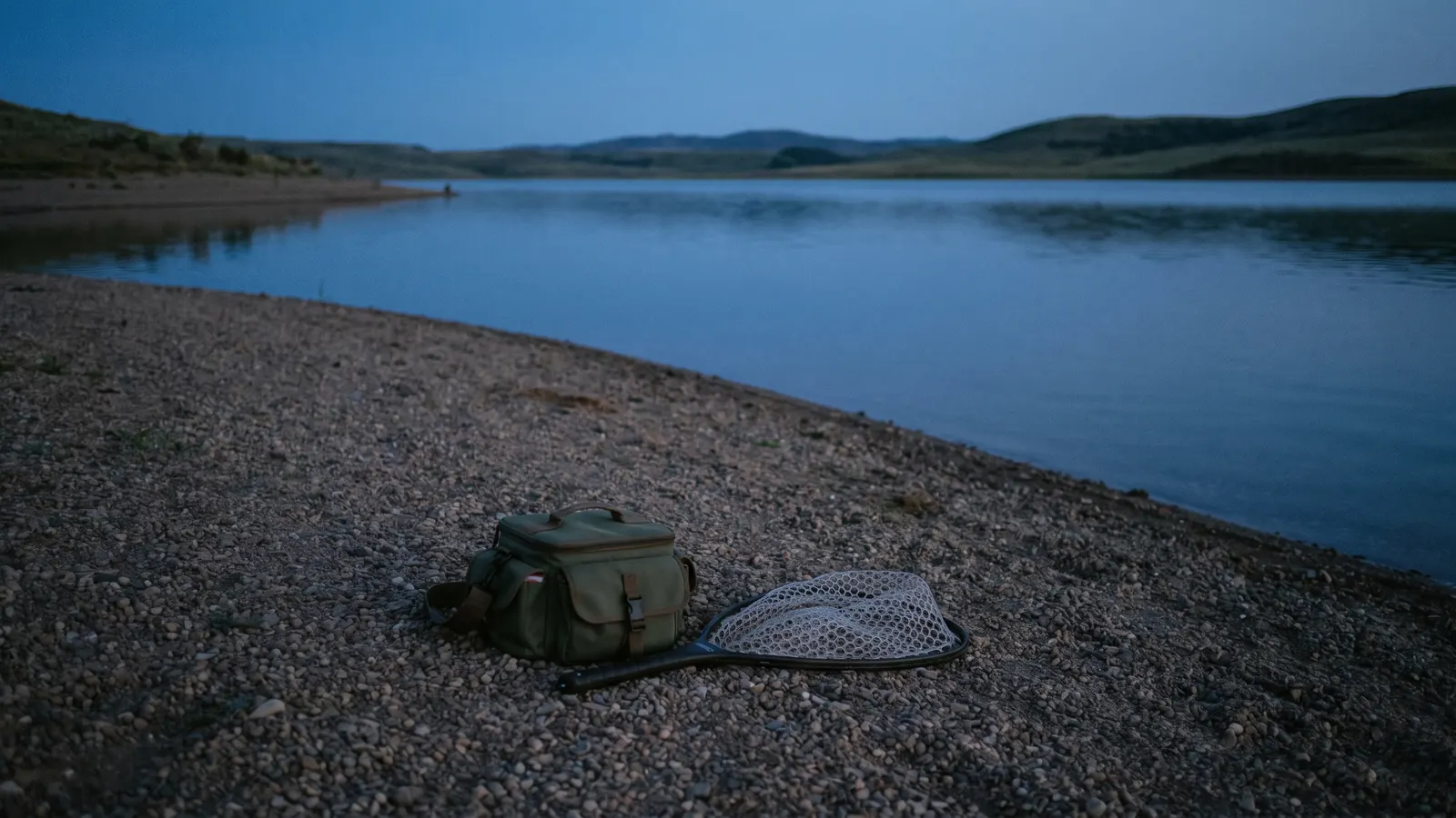 Tackle bag and landing net beside a lake at dusk