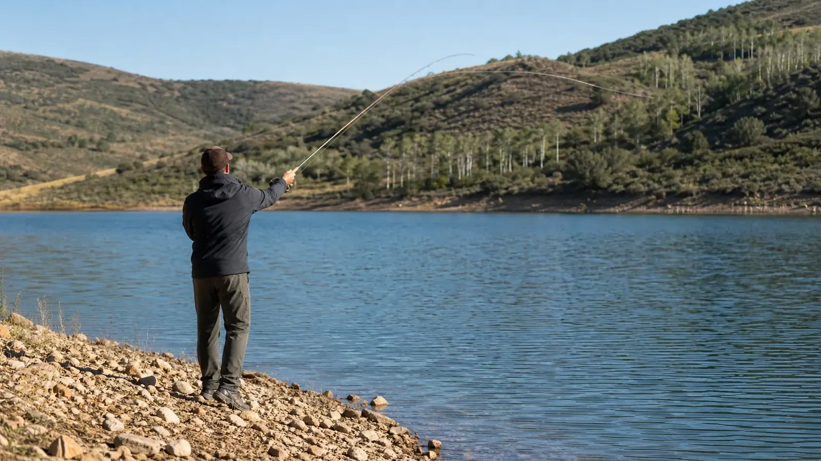 Shore angler casting across a calm reservoir