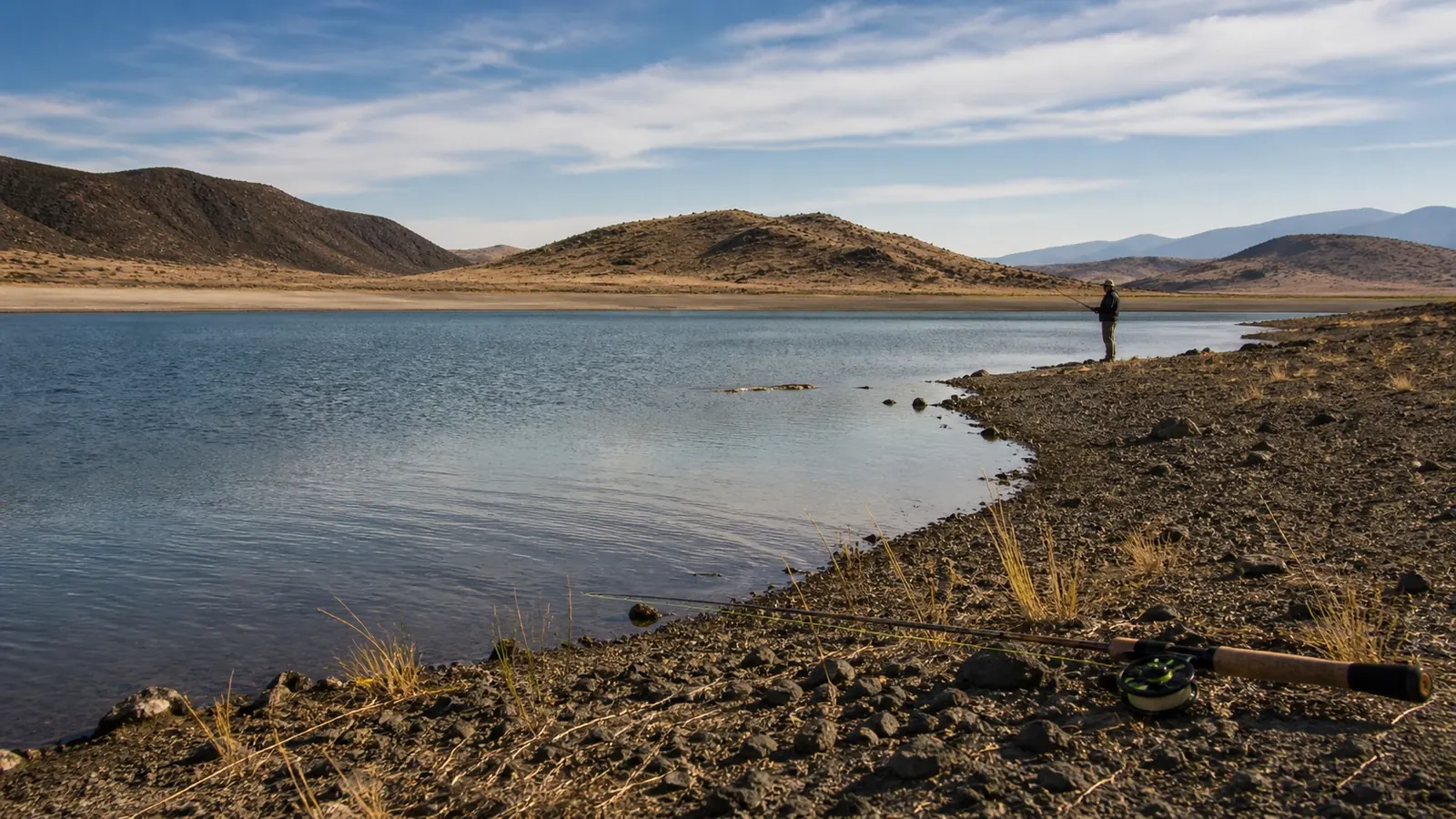 Angler on a gently sloping shoreline below dry hills