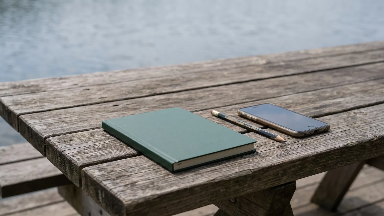 Phone and plain notebook on a lakeside picnic table