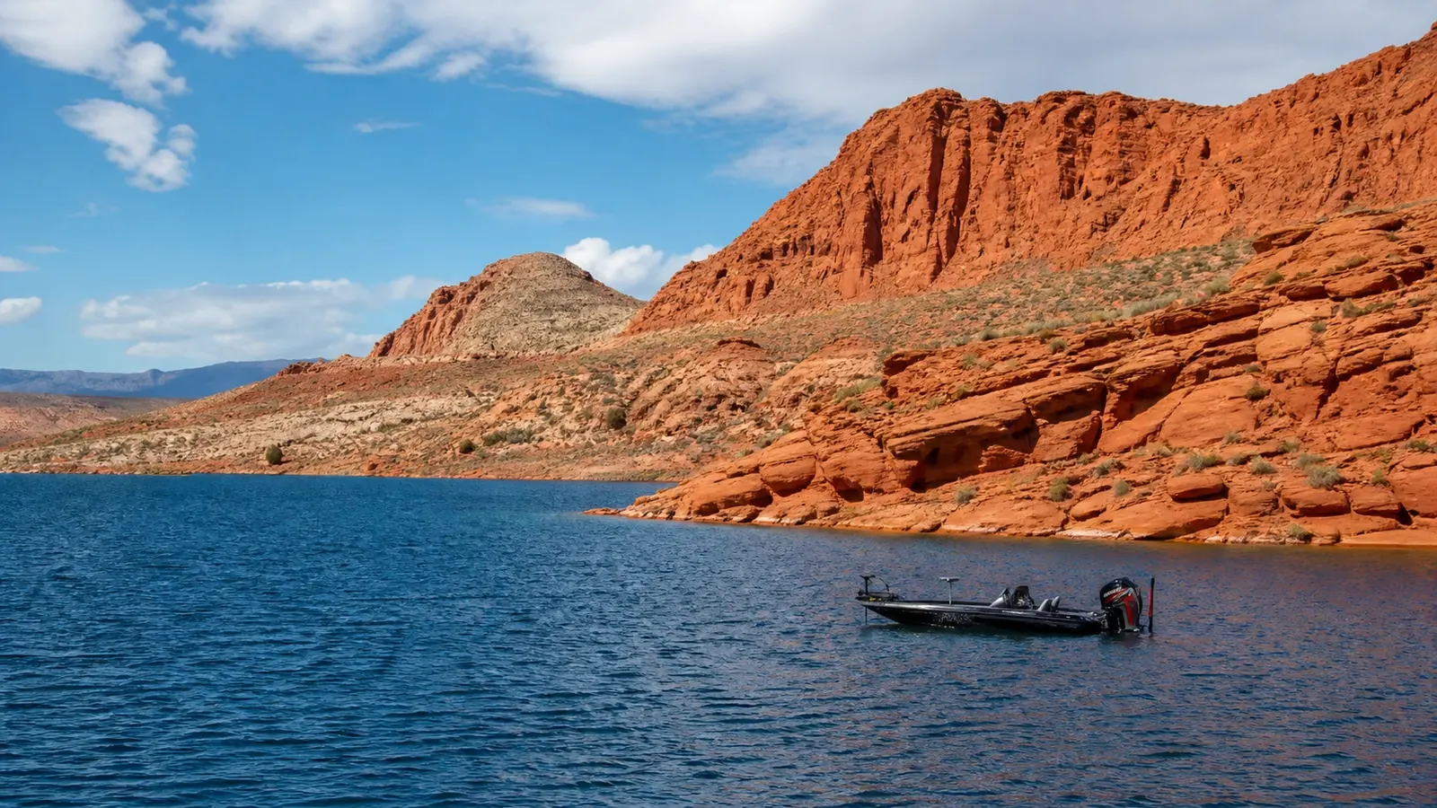 Boat on blue reservoir water beside red sandstone
